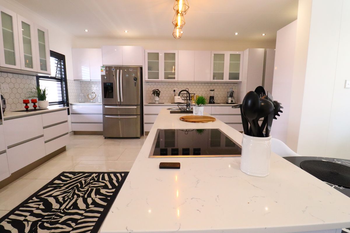 Modern kitchen featuring a central island with a built-in induction hob, white cabinetry, stone countertops, and a tiled backsplash.