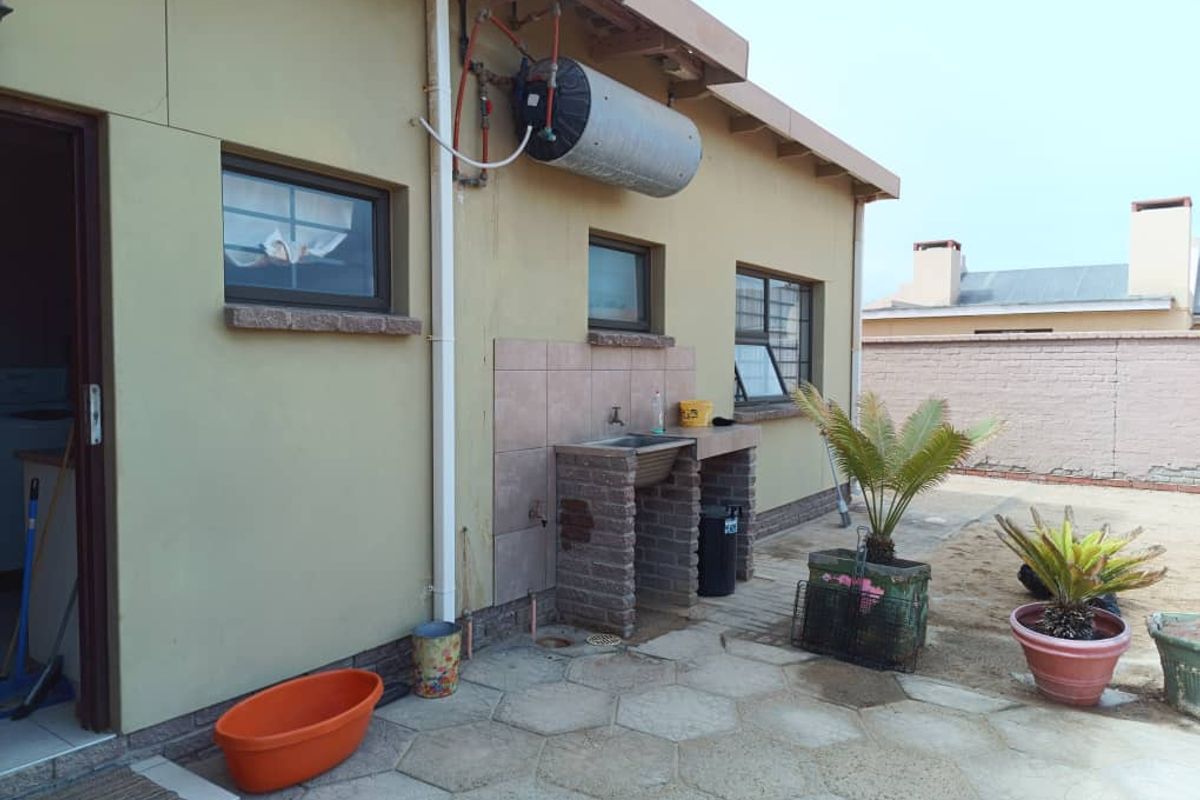 Rear exterior view featuring a paved patio area, a built-in brick utility sink, and an externally mounted electric water heater.