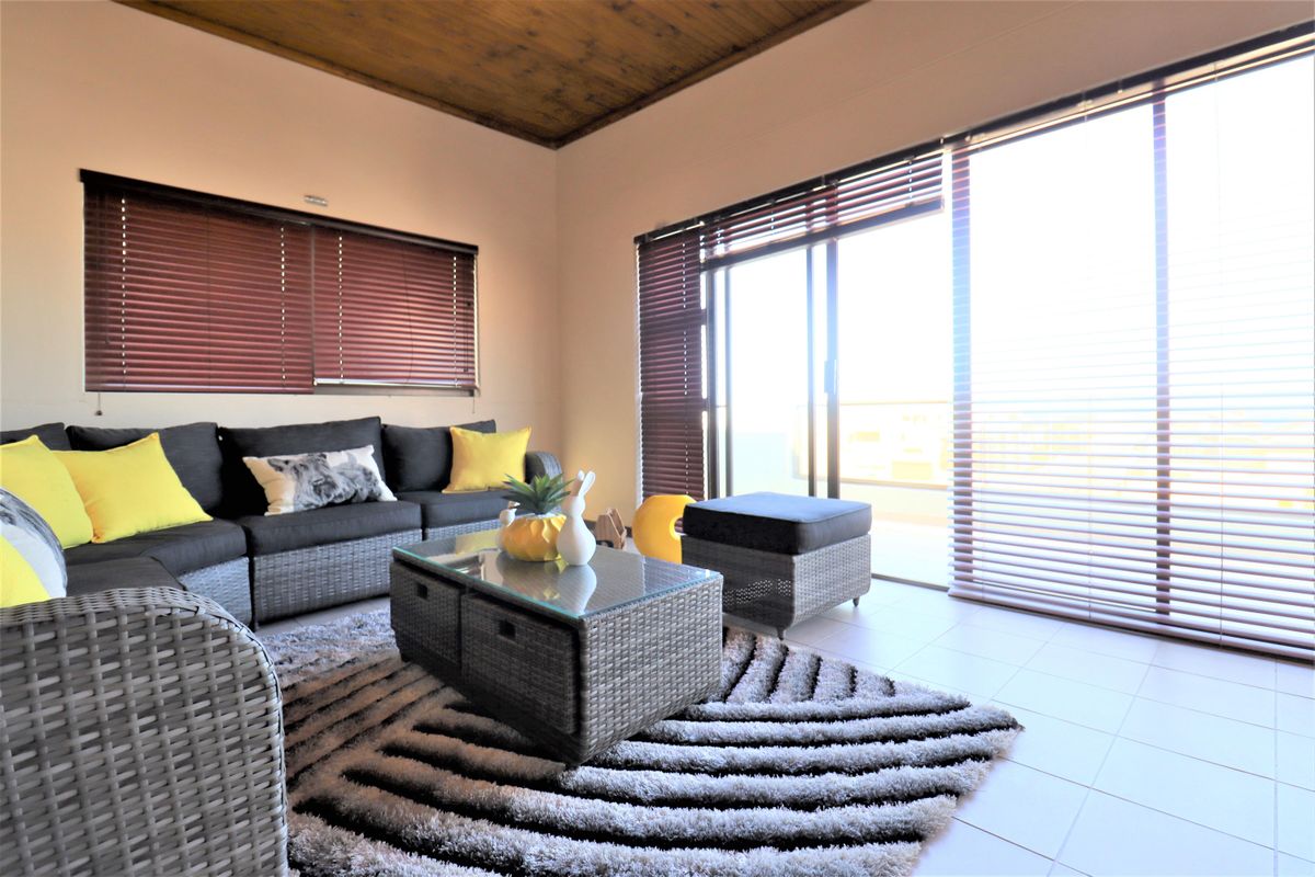A bright living room featuring tiled flooring, a timber-clad ceiling, and large sliding glass doors that provide access to an outdoor area.