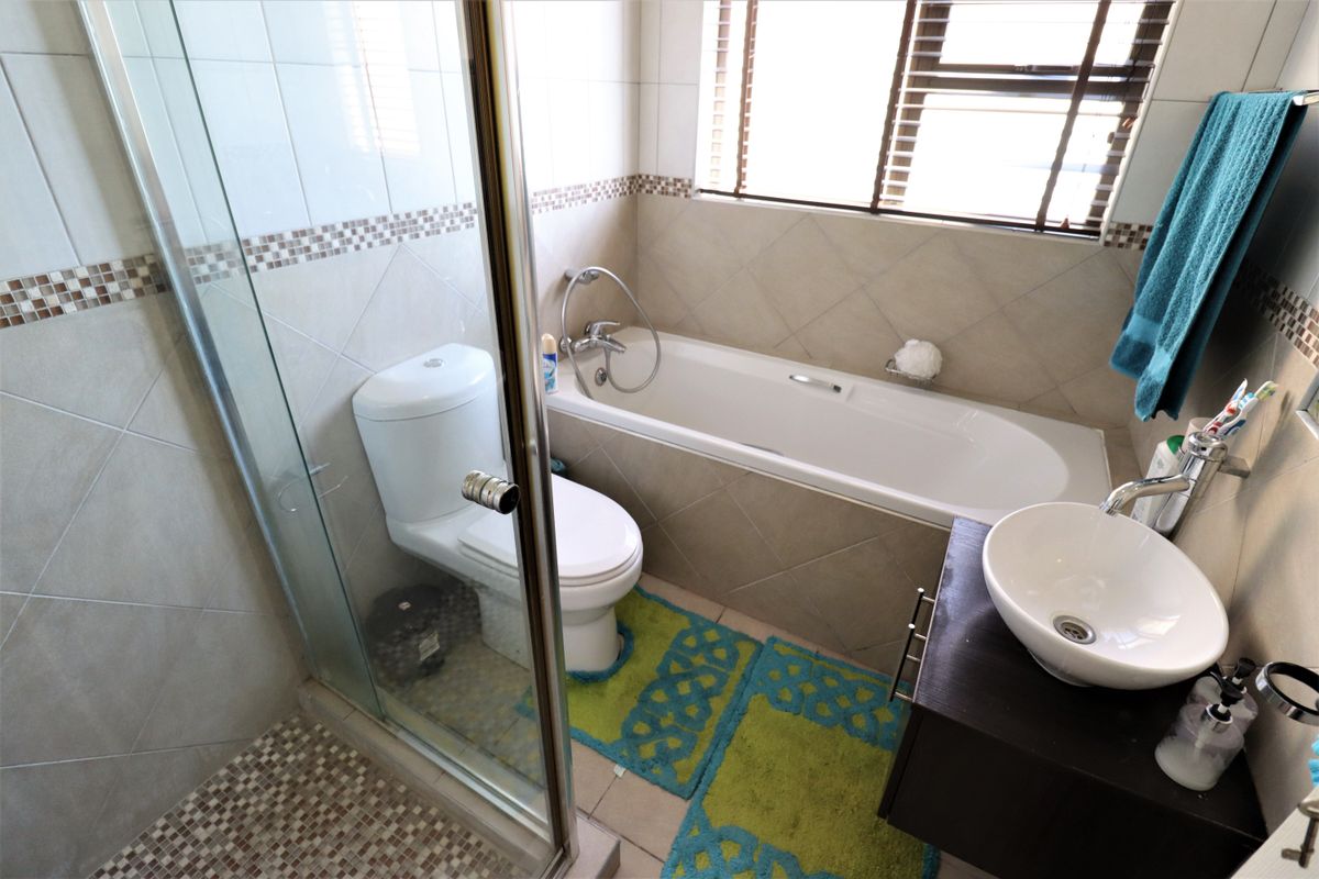 A functional bathroom featuring a glass-enclosed shower, a built-in bathtub, a toilet, and a modern vessel sink vanity with tiled walls.
