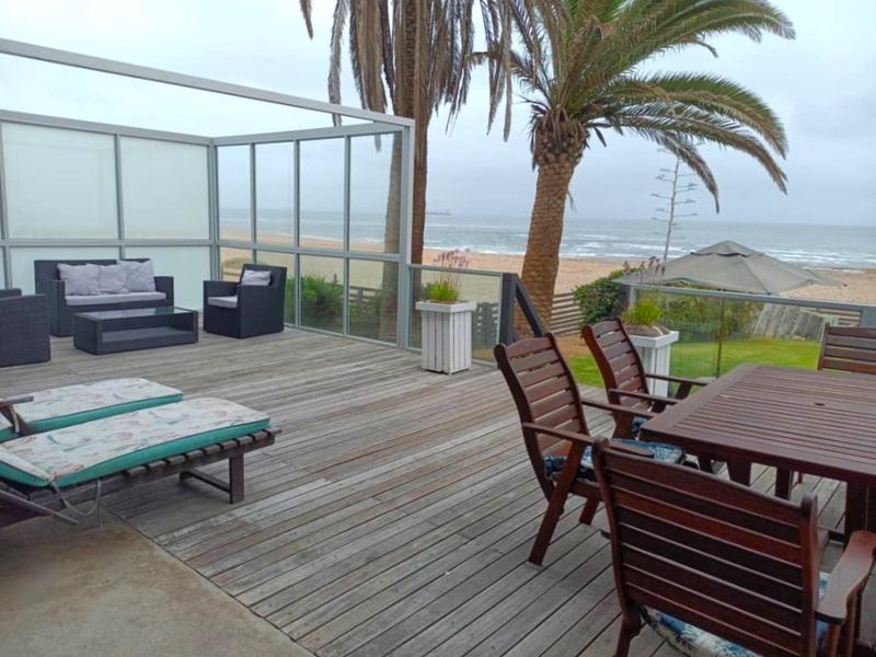 Spacious beachfront timber deck featuring a metal pergola frame, glass balustrades, and direct ocean views, ideal for outdoor entertaining.
