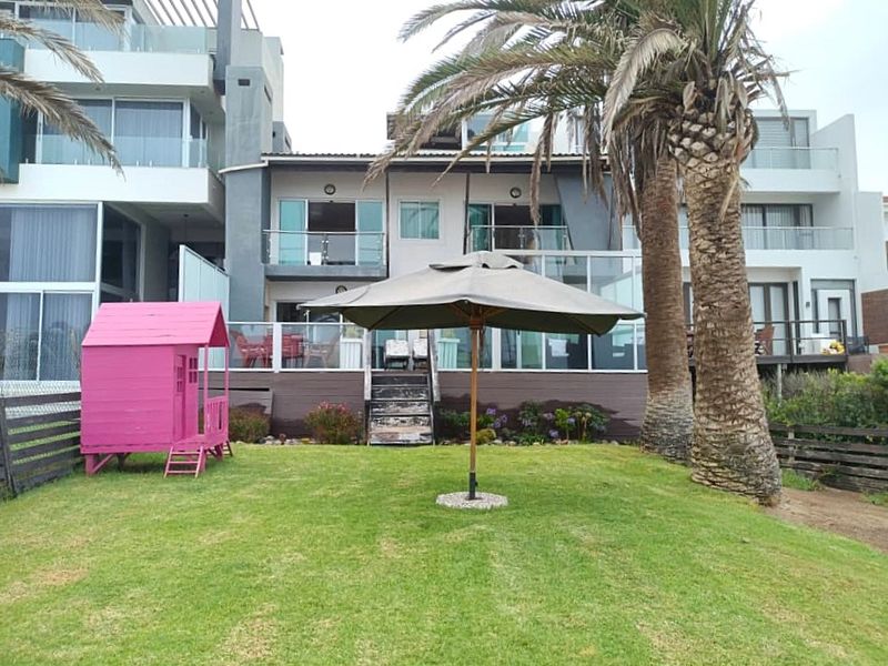 Rear view of a multi-story residential property featuring a raised timber deck with glass balustrades, sliding door access, and a well-maintained lawn area.