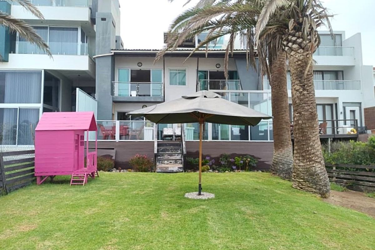 Rear view of a multi-story residential property featuring a raised timber deck with glass balustrades, sliding door access, and a well-maintained lawn area.