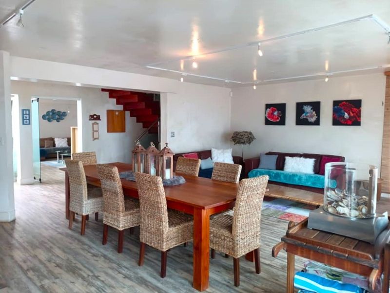 Spacious open-plan living and dining area featuring laminate flooring, track lighting, and an internal staircase leading to the upper level.