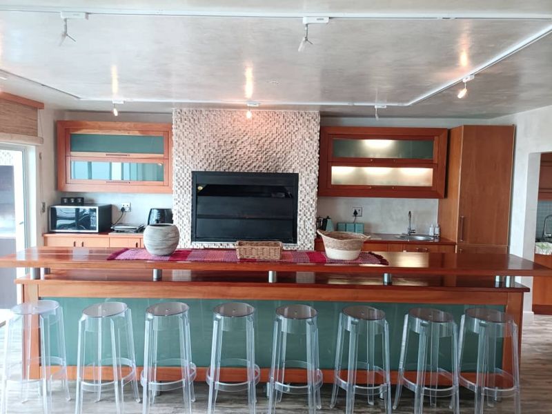 Open-plan entertainment area featuring a built-in braai with a stone mosaic surround, timber cabinetry, and a large wooden breakfast bar.