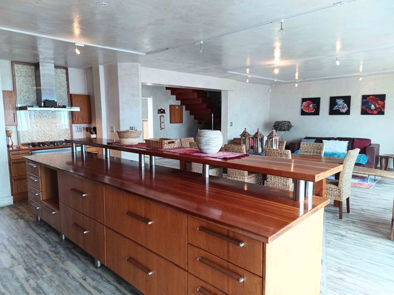 Spacious open-plan living area featuring a large wooden kitchen island, modern cabinetry, track lighting, and a staircase leading to the upper level.