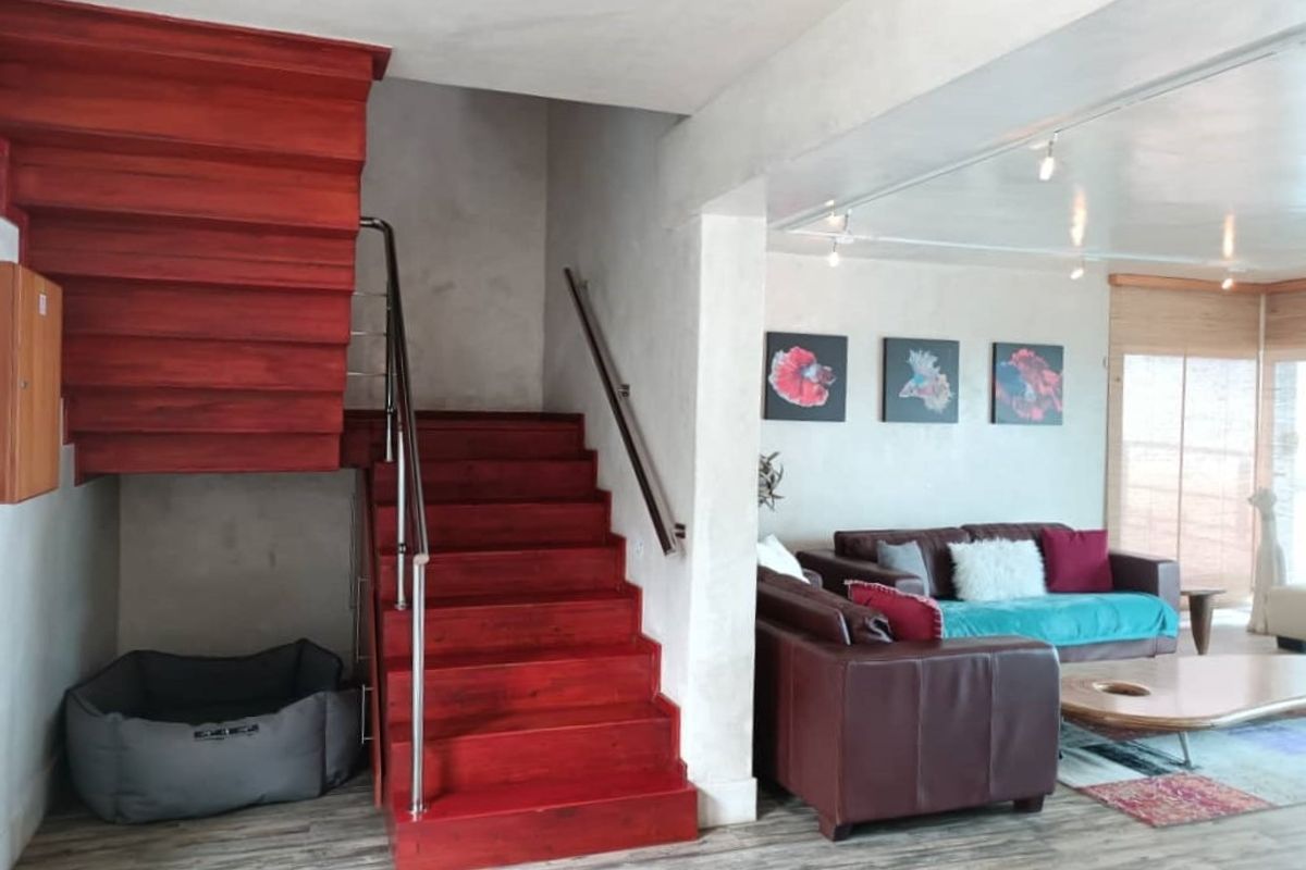 Open plan living area featuring a prominent red wooden staircase with stainless steel handrails and modern recessed ceiling lighting.