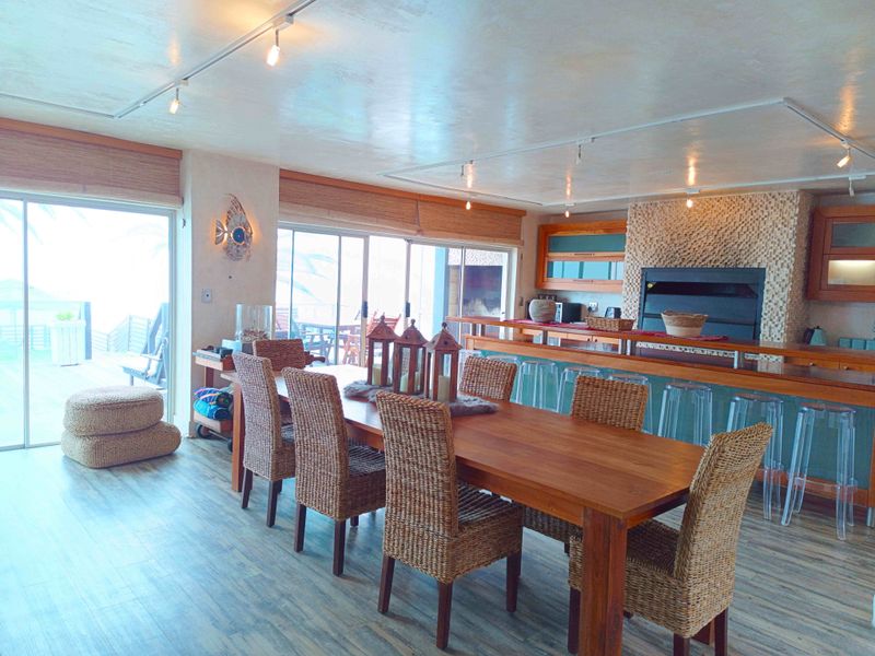 Spacious open-plan living and dining area featuring a built-in braai, breakfast bar, track lighting, and large sliding doors leading to an outdoor patio.