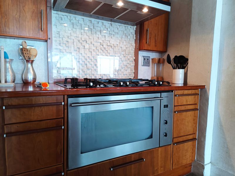 A well-maintained kitchen featuring wooden cabinetry, a built-in oven, gas cooktop, extractor fan, and a unique textured stone splashback.