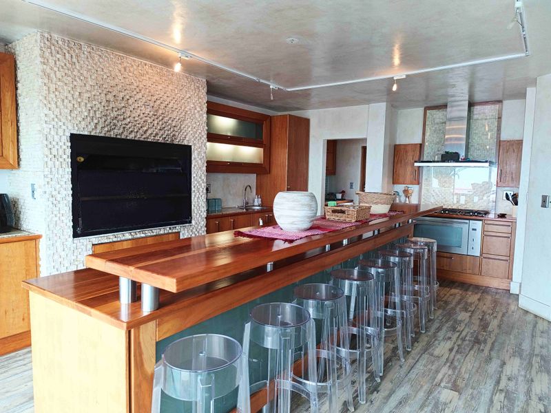 Spacious open-plan kitchen and living area featuring a large wooden breakfast bar, built-in fireplace with stone cladding, and modern cabinetry.