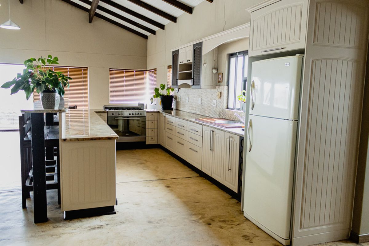 Spacious kitchen featuring cream cabinetry, granite countertops, a built-in gas stove, and vaulted ceilings with exposed timber beams.