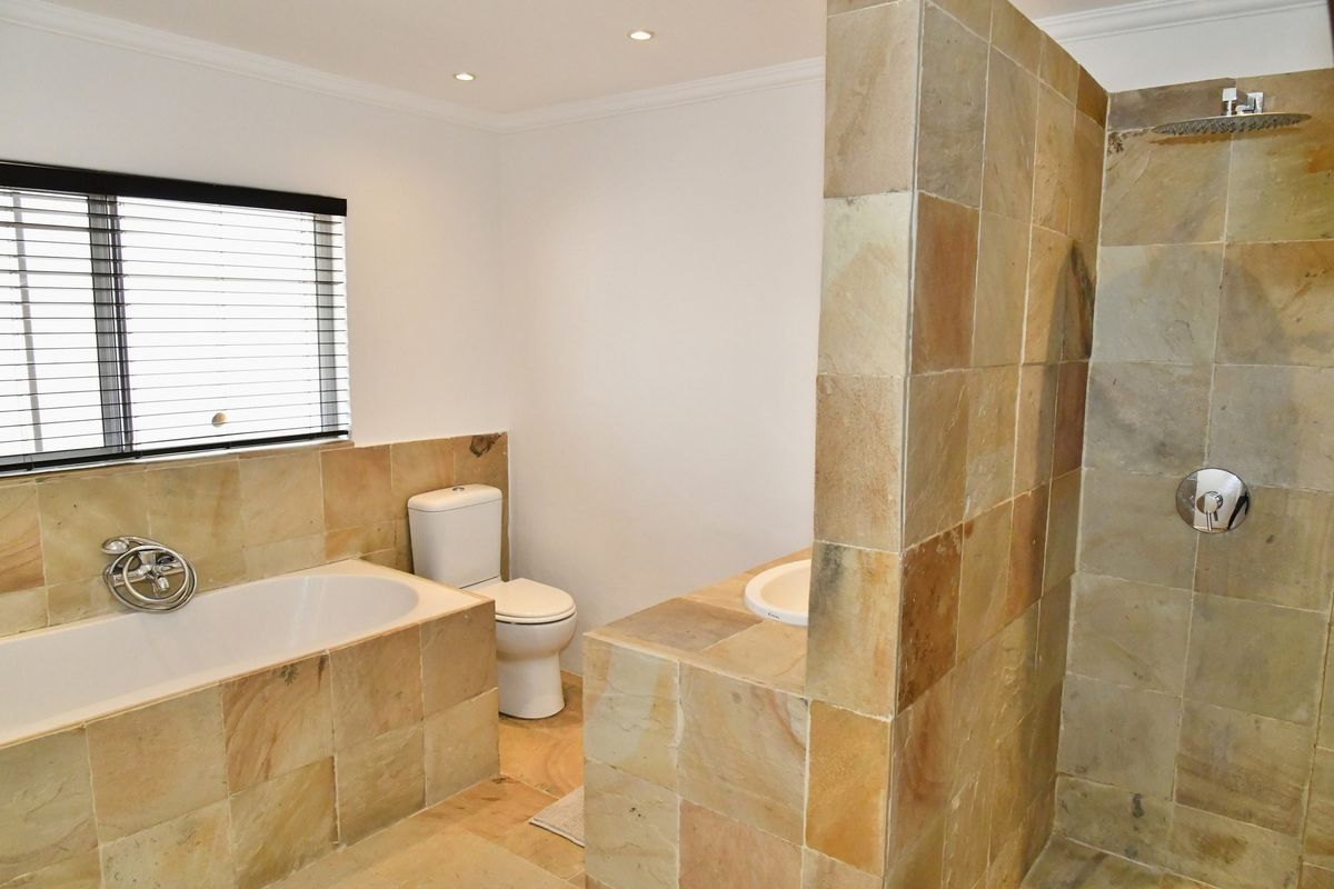 A bathroom featuring a built-in bathtub, a separate shower enclosure with stone-style tiling, and a toilet, finished with neutral wall tones.