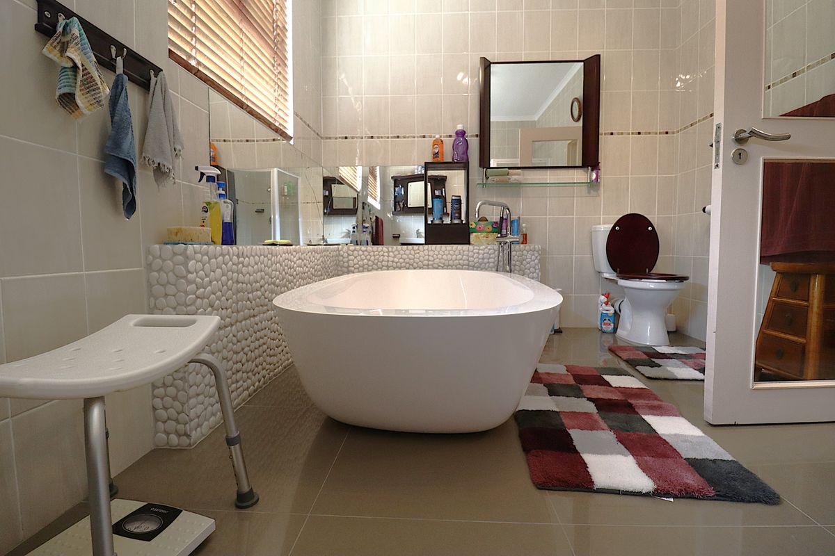 A bathroom featuring a freestanding bathtub with a pebble-tiled surround, a wall-mounted toilet, and tiled walls.