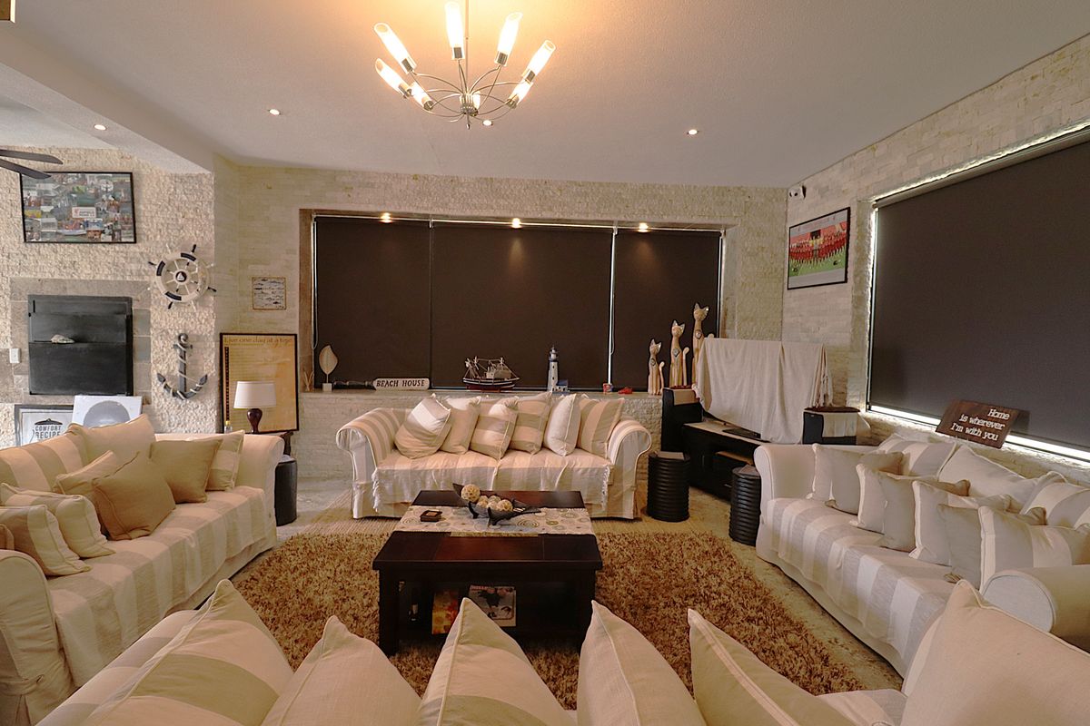 Spacious living room featuring textured stone feature walls, recessed downlighting, a modern chandelier, and large windows with fitted roller blinds.