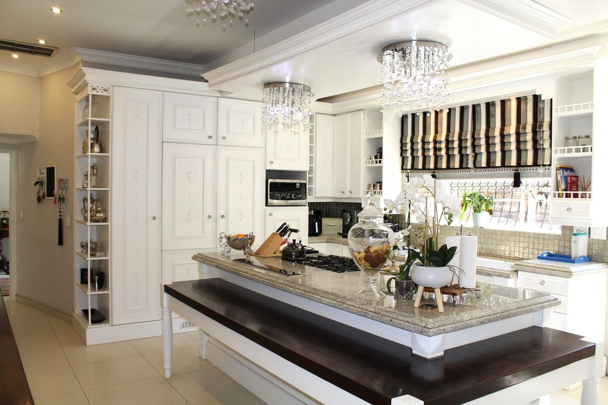 A well-appointed kitchen featuring white cabinetry, granite countertops, a central island with integrated hob, and elegant crystal light fixtures.