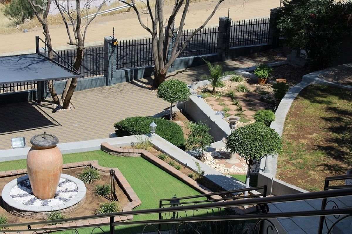 A landscaped rear garden featuring tiered retaining walls, paved patio areas, artificial lawn sections, and a decorative central water feature.