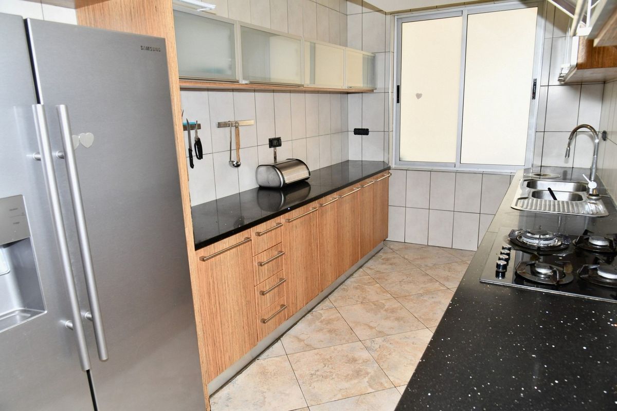 A functional kitchen featuring wood-grain cabinetry, black granite countertops, a built-in gas hob, and tiled flooring.