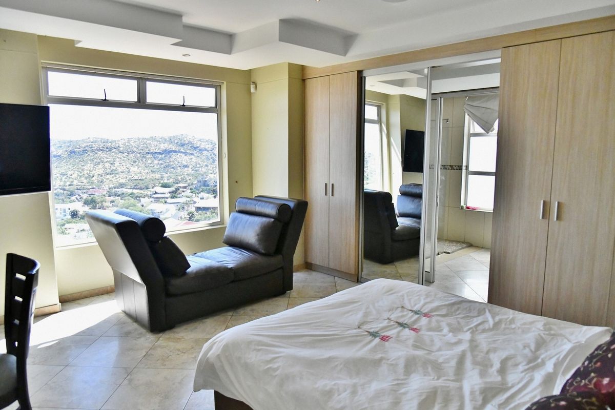 A spacious bedroom featuring built-in wooden wardrobes, tiled flooring, and large windows offering expansive scenic views, with an integrated en-suite bathroom area.