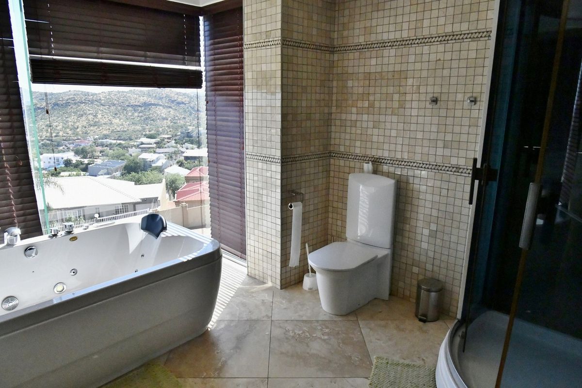 Modern bathroom featuring a jetted soaking tub, a separate shower, and a toilet, complemented by floor-to-ceiling tiled walls and expansive scenic views.