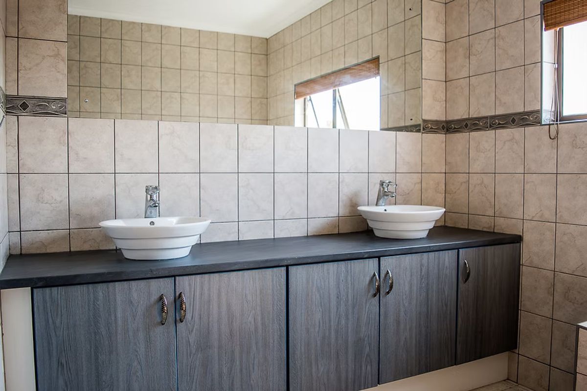 A well-maintained bathroom featuring a double vanity with vessel sinks, dark wood-look cabinetry, and full-wall tiling.