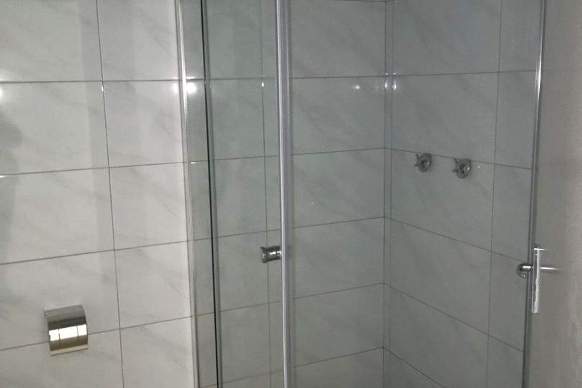 A modern bathroom shower enclosure featuring glass panels, chrome fixtures, and marble-look wall tiling with a mosaic-tiled shower floor.