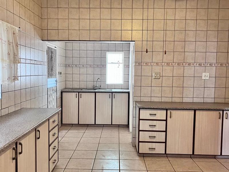 A spacious, functional kitchen featuring extensive tiled wall finishes, ample laminate cabinetry, granite countertops, and a central ceiling fan.