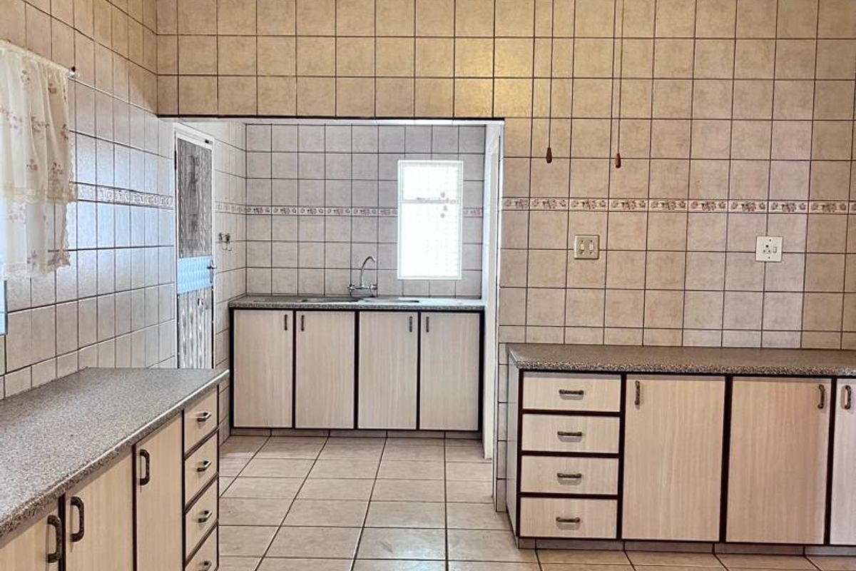 A spacious, functional kitchen featuring extensive tiled wall finishes, ample laminate cabinetry, granite countertops, and a central ceiling fan.