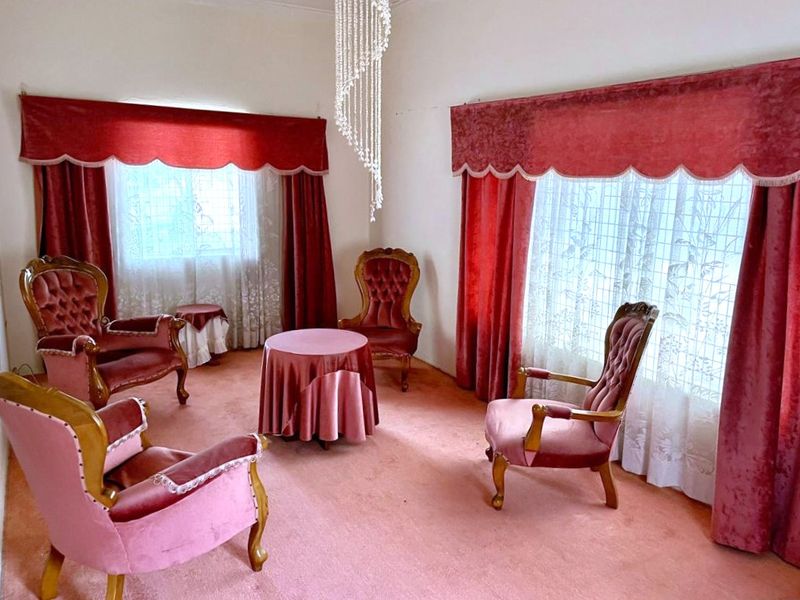 A formal living room featuring a crystal chandelier and wall-to-wall carpeting, offering a traditional layout with ample natural light from large windows.