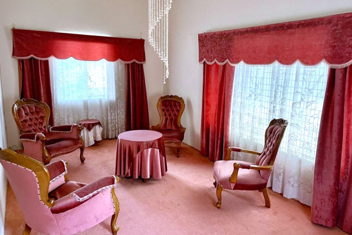 A formal living room featuring a crystal chandelier and wall-to-wall carpeting, offering a traditional layout with ample natural light from large windows.
