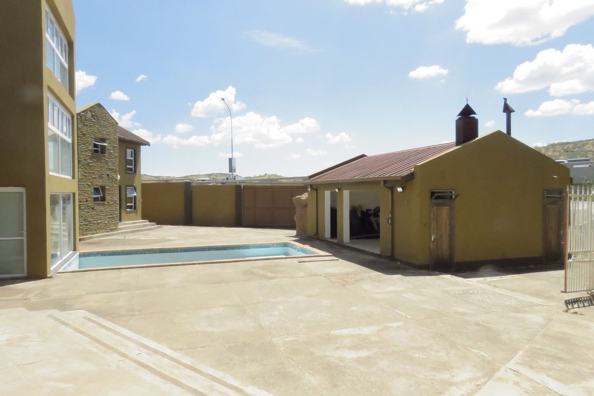 Spacious outdoor area featuring a swimming pool, paved courtyard, and a detached outbuilding with a chimney, set against a multi-story residential structure.
