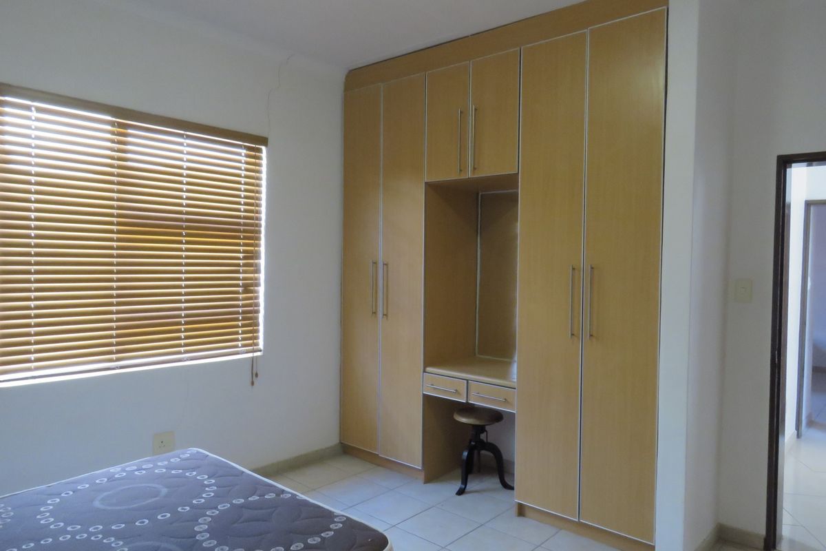 A bedroom featuring built-in wooden cabinetry with an integrated vanity desk, tiled flooring, and window blinds.