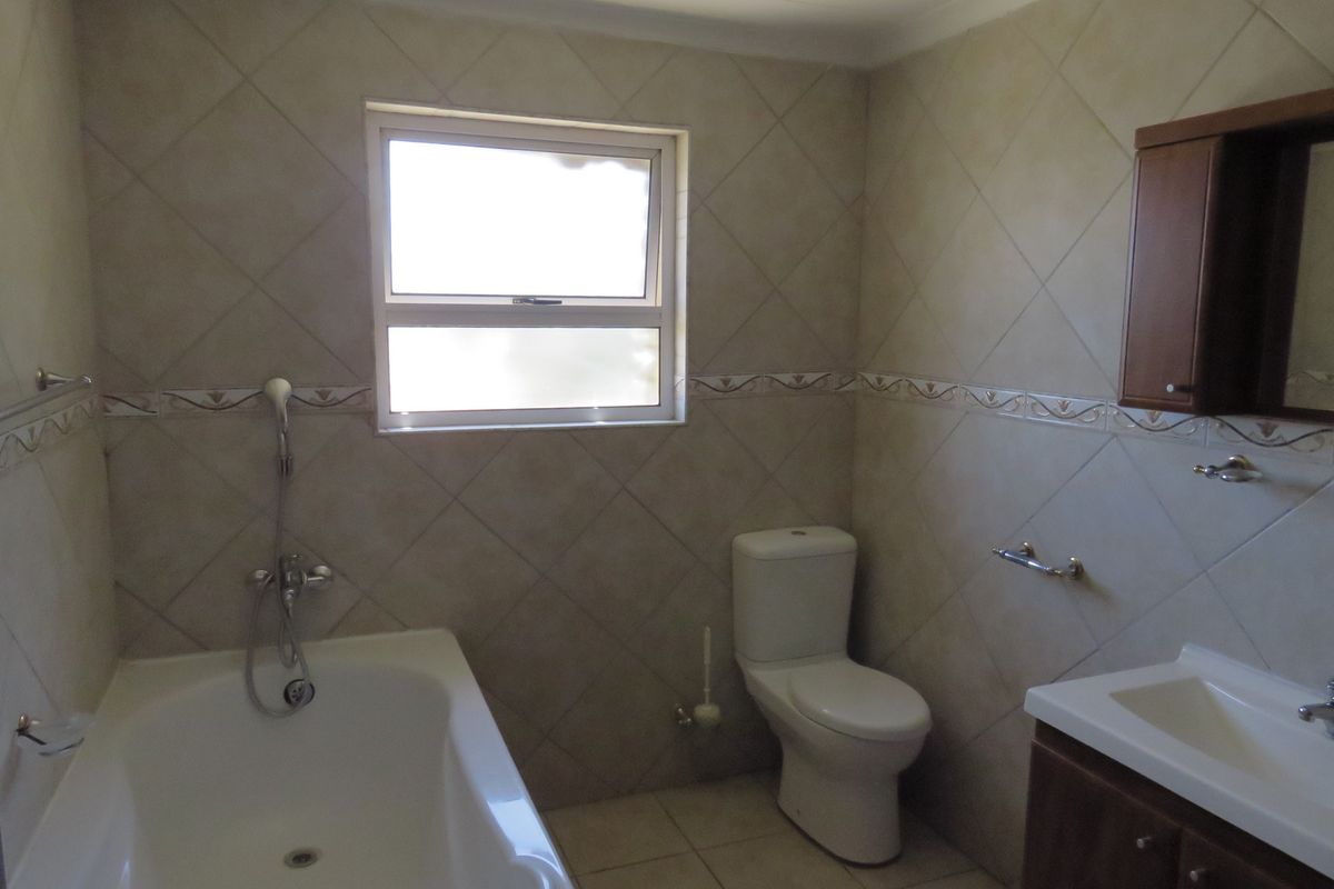 A functional bathroom featuring a built-in bathtub with shower mixer, a standard toilet, and a vanity cabinet with a basin.