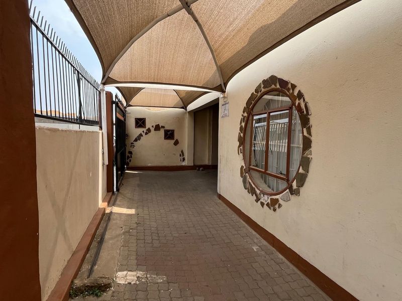 A covered driveway area featuring a shade sail, paved flooring, and a distinctive circular window set into the exterior wall.
