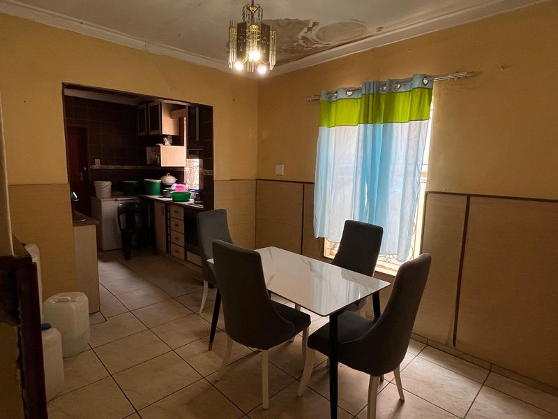 Open plan dining and kitchen area featuring tiled floors and dated finishes, currently showing signs of ceiling water damage and wall wear.