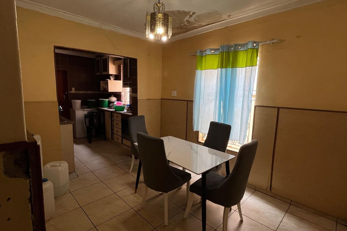 Open plan dining and kitchen area featuring tiled floors and dated finishes, currently showing signs of ceiling water damage and wall wear.