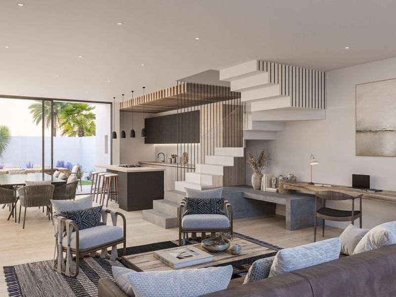 Modern open-plan living area featuring a sleek kitchen, integrated staircase, built-in desk, and seamless flow to the outdoor patio through large sliding glass doors.