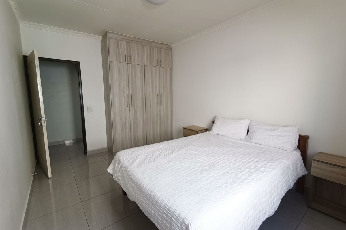 A well-maintained bedroom featuring neutral tiled flooring, built-in wooden cabinetry, and decorative ceiling cornicing.