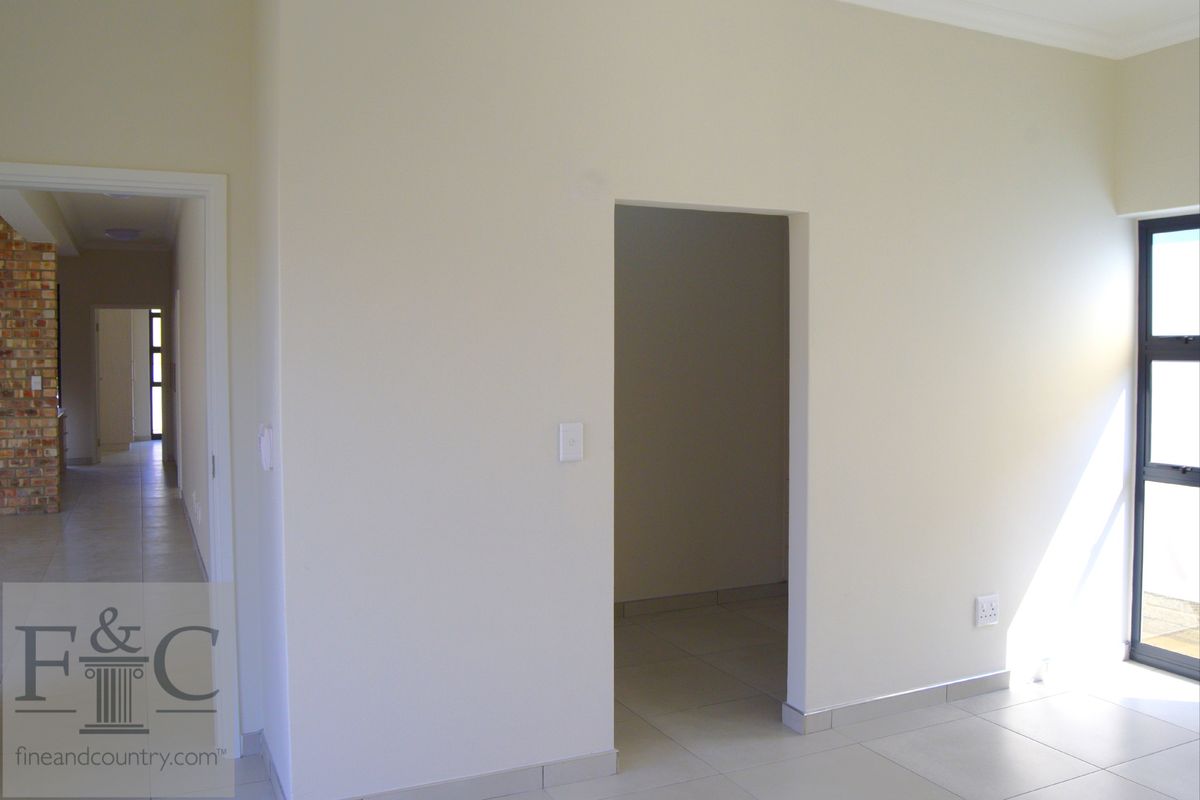 An interior view of a neutral-toned living space featuring tiled flooring, a doorway leading to an adjacent room, and a large window.