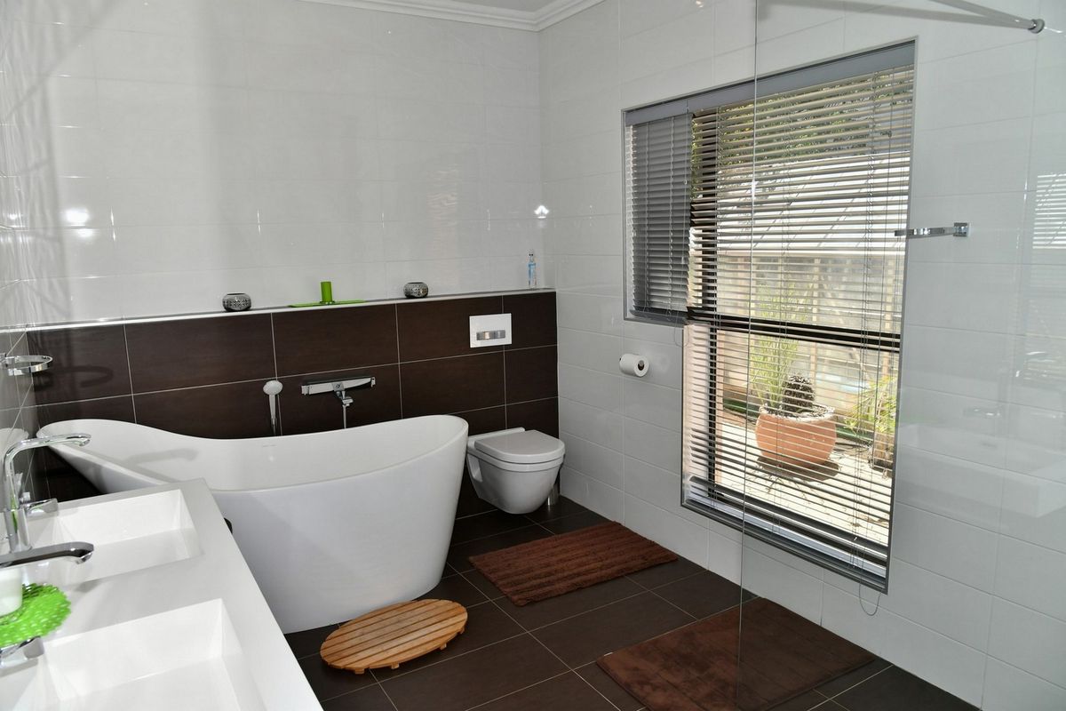 Modern bathroom featuring a freestanding bathtub, wall-mounted toilet, and double vanity with contemporary tiling and large window.