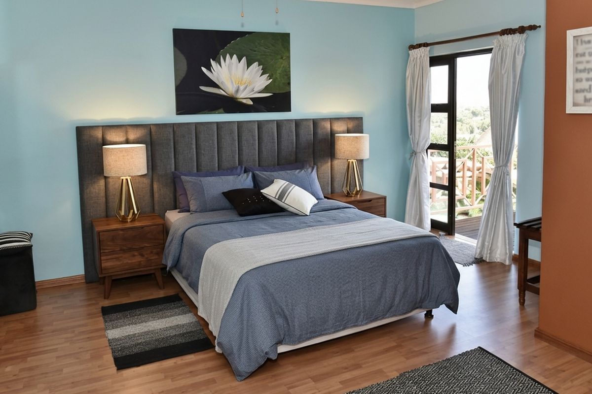 A well-maintained bedroom featuring laminate flooring, a built-in headboard, and direct access to an outdoor balcony through a glass-paneled door.
