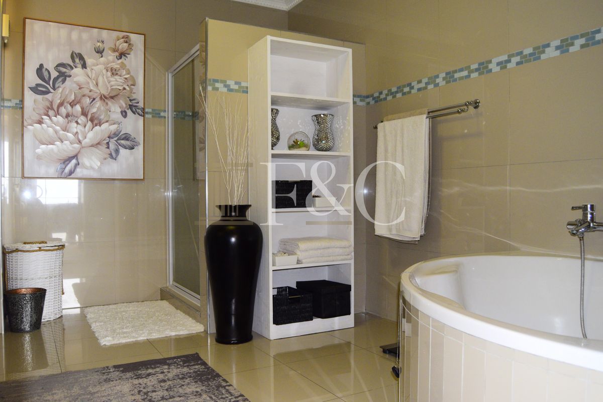 A well-maintained bathroom featuring a corner bathtub, a glass-enclosed shower, and neutral wall tiling with a decorative mosaic border.