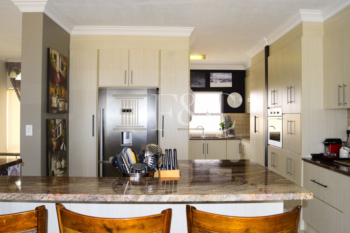 A well-appointed kitchen featuring light wood-grain cabinetry, granite countertops, a breakfast bar, and integrated stainless steel appliances including an oven and refrigerator.