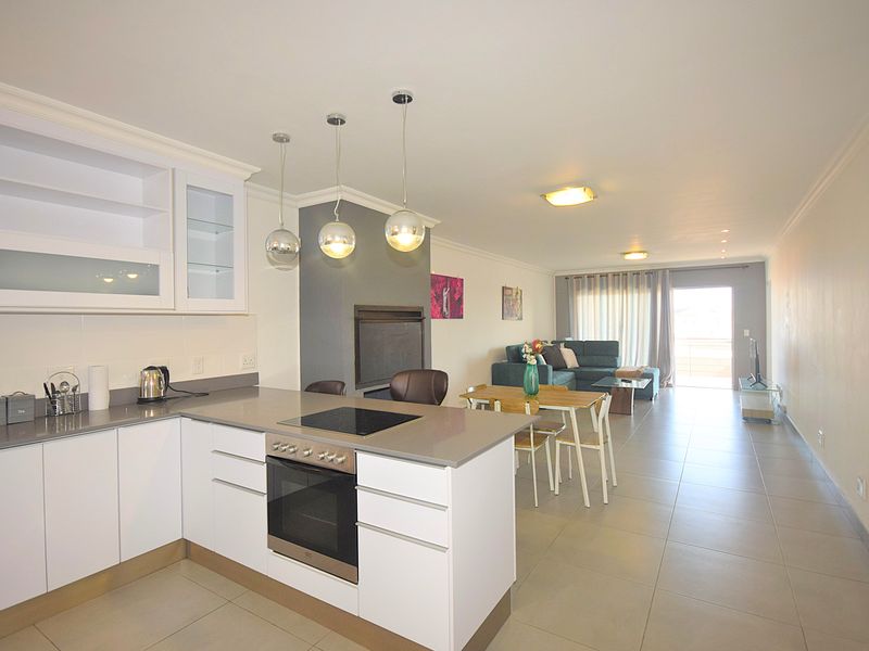 Open-plan living area featuring a modern kitchen with built-in oven, hob, and stone countertops, flowing into a spacious lounge with access to a balcony.