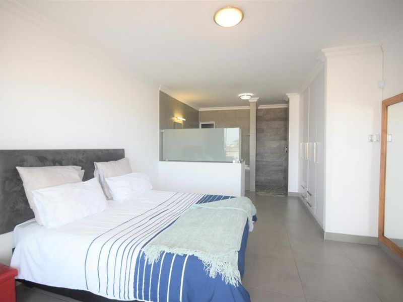 Spacious bedroom featuring built-in cupboards, tiled flooring, and an open-plan en-suite bathroom with a modern walk-in shower.