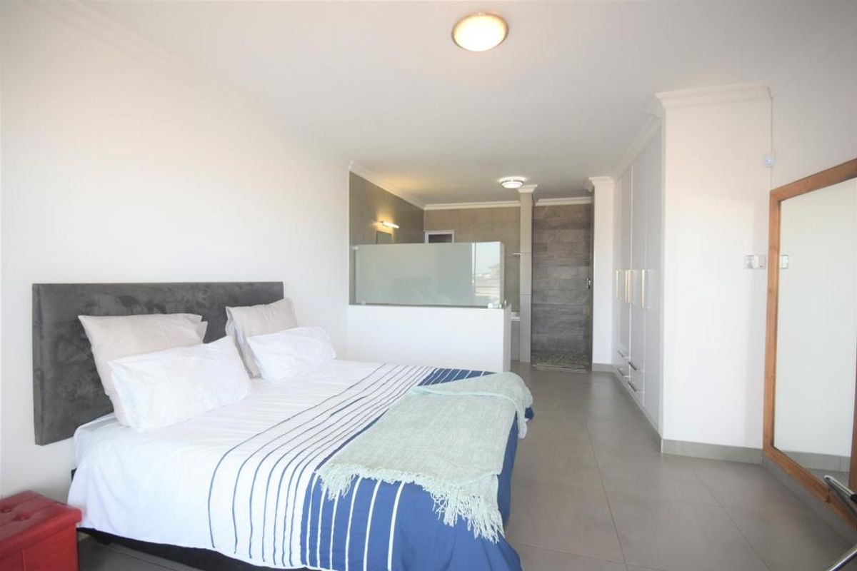 Spacious bedroom featuring built-in cupboards, tiled flooring, and an open-plan en-suite bathroom with a modern walk-in shower.