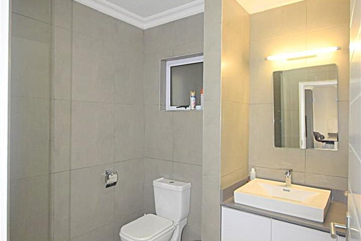 Modern bathroom featuring a wall-mounted vanity with basin, glass-enclosed shower, and neutral floor-to-ceiling tiling.