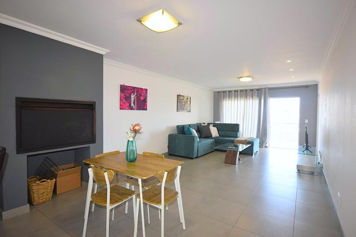 Spacious open-plan living and dining area featuring large format floor tiles, a built-in fireplace, and sliding door access to a balcony.
