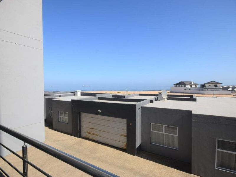 View from an elevated balcony overlooking a coastal residential area with a clear view of the ocean and nearby properties.