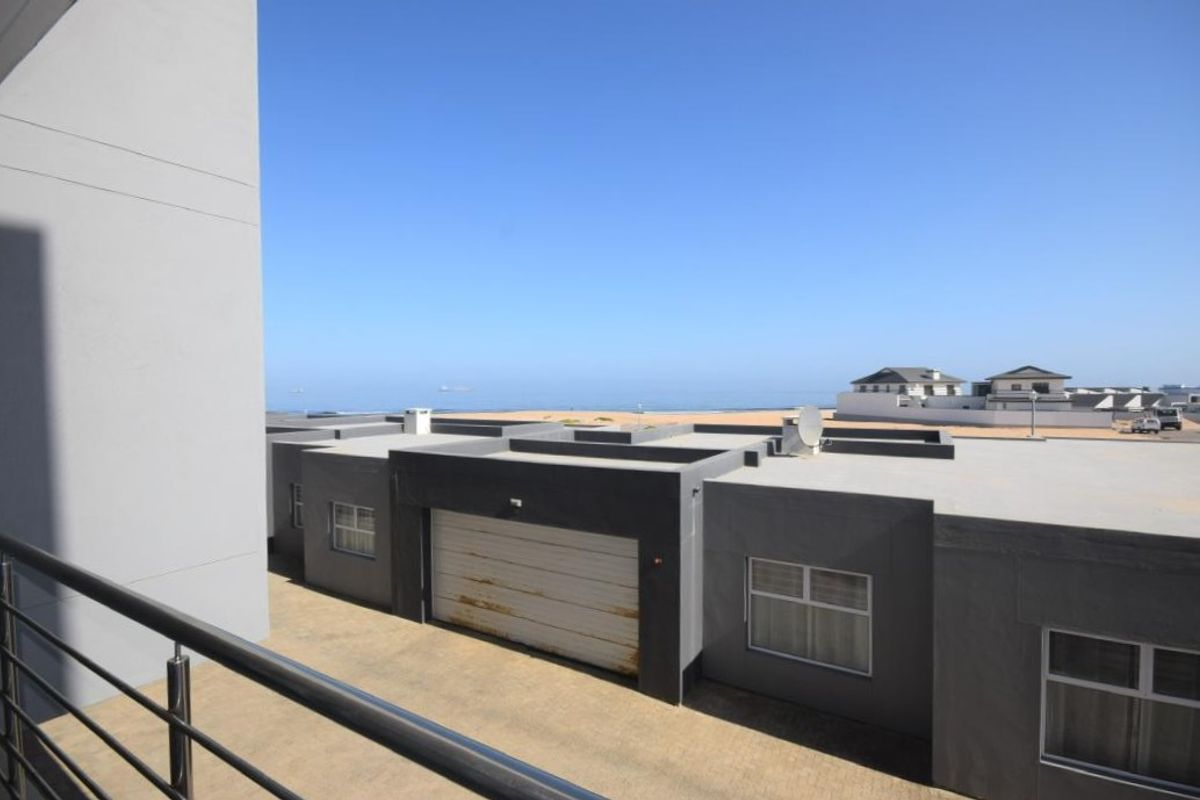 View from an elevated balcony overlooking a coastal residential area with a clear view of the ocean and nearby properties.