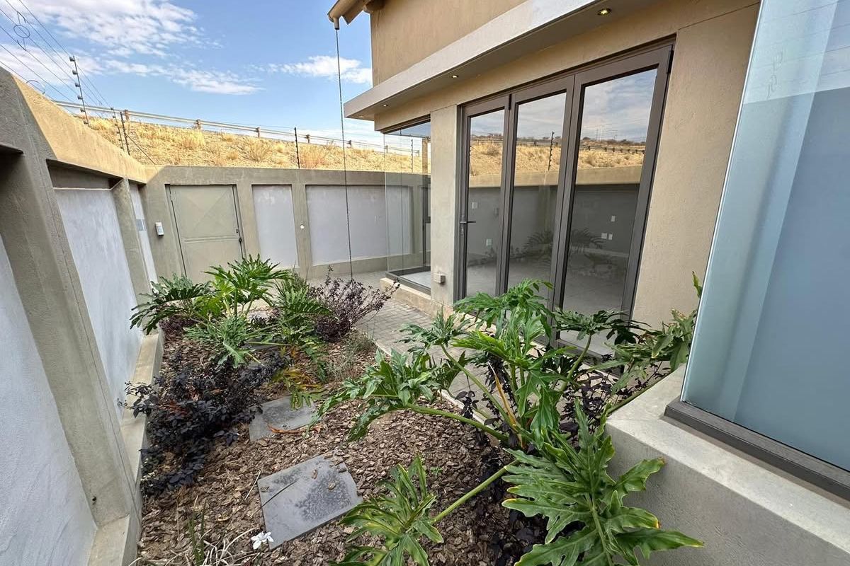 A private rear courtyard featuring paved pathways, landscaped garden beds, and modern aluminium-framed glass doors providing access to the home.